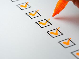 orange pen ticking off items on paper list